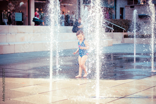 Cute Little Girl in Blue Swimming Suit Playing with Water jets of Street Fountain, Hot Summer Day, Kids Fun, in England, Dorchester