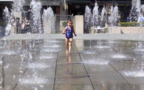 Cute Little Girl in Blue Swimming Suit Playing with Water jets of Street Fountain, Hot Summer Day, Kids Fun, in England, Dorchester