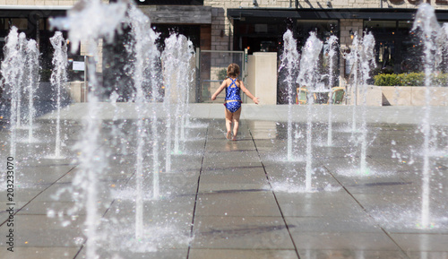 Cute Little Girl in Blue Swimming Suit Playing with Water jets of Street Fountain, Hot Summer Day, Kids Fun, in England, Dorchester