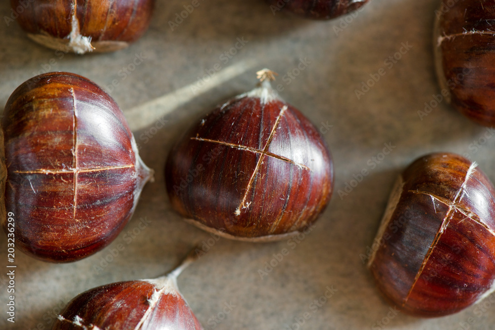 Chestnuts being prepared for baking with a knife-cut cross on top of each nut 