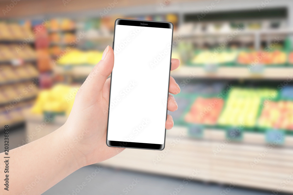 Female hand holding black phone with isolated screen, grocery store in background. Online shopping concept, Mockup Female hand holding black phone with isolated screen, grocery store in background. Online shopping concept, Mockup