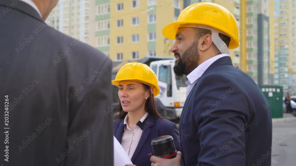 three serious business man at a construction site against a truck background. Men and woman in suits and yellow helmets. 4k three serious business man at a construction site against a truck background. Men and woman in suits and yellow helmets. 4k