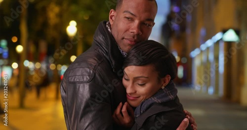 African boyfriend and girlfriend hold each other tightly on a romantic evening out in Paris, Young African-American couple hugging each other warmly on the Champs-Elysees 