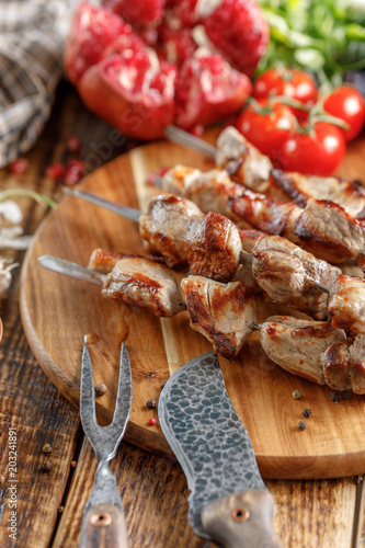Tasty and juicy kebabs of pork on a wooden board with original cutlery.