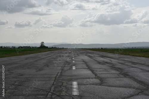 Abandoned runway used as rally racetrack. Cracks and car tire tracks seen on the wet after the spring rain asphalt surface. 