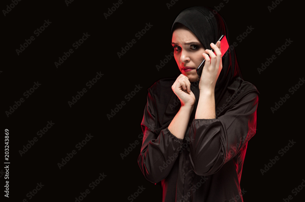 Portrait of beautiful serious scared frightened young woman wearing black hijab calling for help on black background Portrait of beautiful serious scared frightened young woman wearing black hijab calling for help on black background