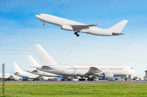 Passenger aircraft row, airplane parked on service before departure at the airport, other plane push back tow. Airplane take off from the runway in the blue sky