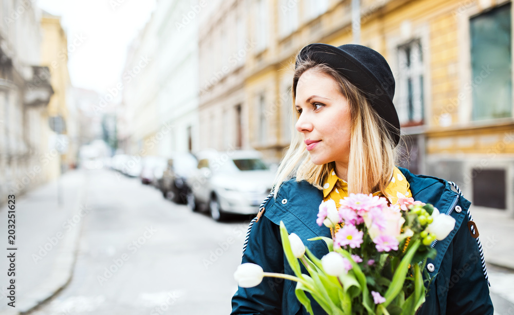 Fototapeta premium Young woman with flowers in sunny spring town.