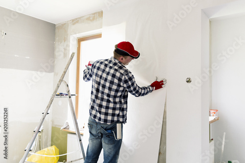 Glueing wallpapers at home. Young man, worker is putting up wallpapers on the wall. Home renovation concept