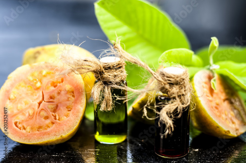 Red and Green colored Floral and fruit essence of Guava or Jamrudh or Psidium guajava or common red guava with its fresh leaves and organic fruit on black wooden surface. photo