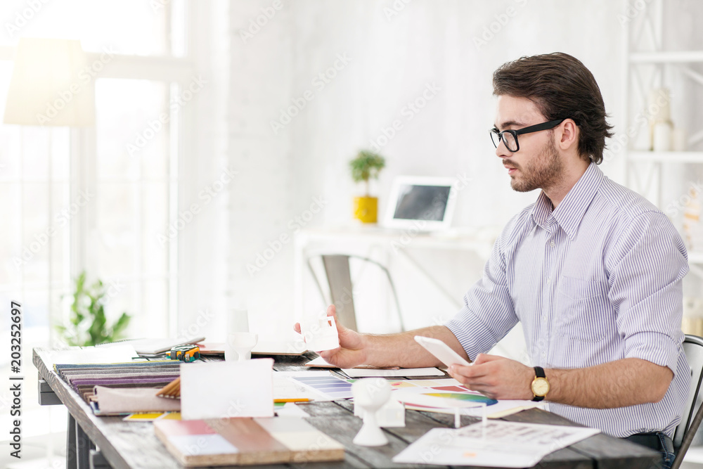 Busy with work. Concentrated bearded manager holding his phone and looking at white object Busy with work. Concentrated bearded manager holding his phone and looking at white object
