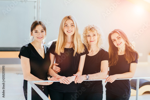 Group of four different ages charming female pilates instructor wear black sportswear in premium modern pilates studio. Sport, fitness, lifestyle, gesture and team work concept. photo