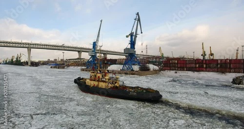 Flying over cargo port. The tugboat moving through an ice. Aerial drone footage