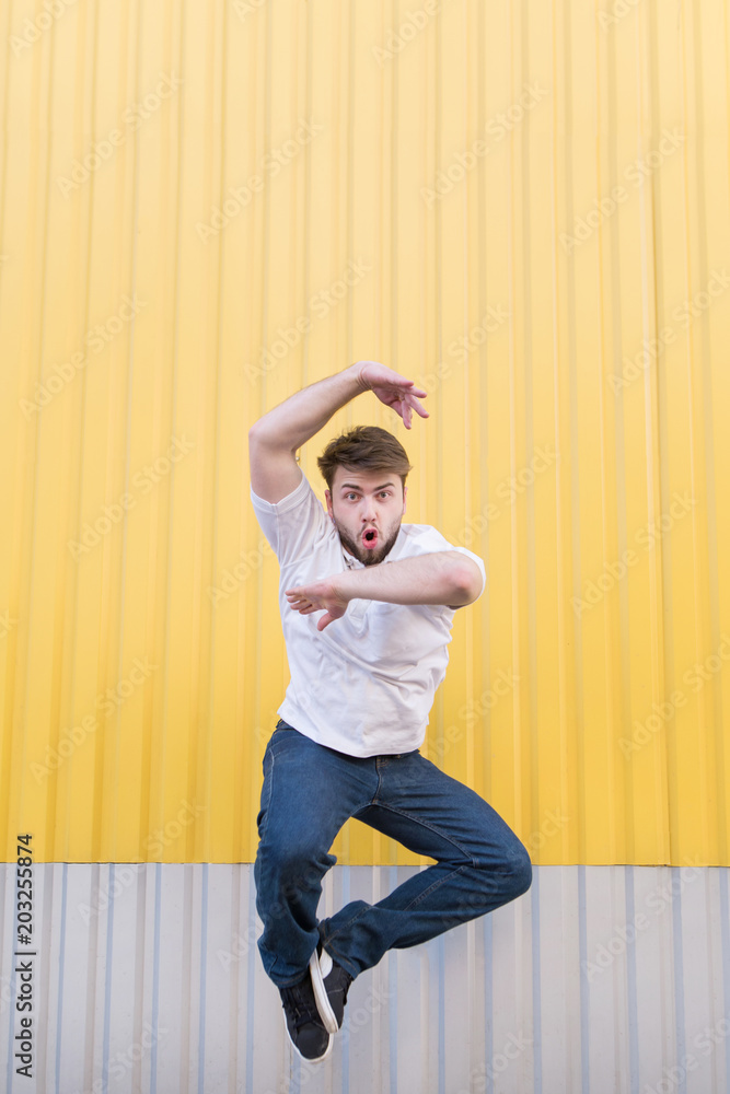 Funny man jumping against the background of the yellow wall and looking at  the camera. Stock Photo | Adobe Stock
