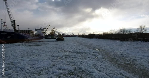 Flying over cargo port. The tugboat moving through an ice. Aerial drone footage
