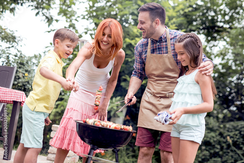 Family having a barbecue party,standing around the grill.