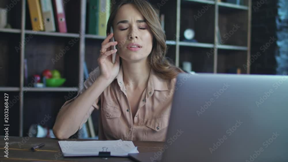 Frustrated woman talking on mobile phone. Business lady working in startup office. Disappointed woman working on business project on laptop. Close up of female specialist speaking phone at workplace Frustrated woman talking on mobile phone. Business lady working in startup office. Disappointed woman working on business project on laptop. Close up of female specialist speaking phone at workplace