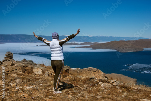 happy traveler girl with raised hands standing on top of a mountain above lake in the spring holiday