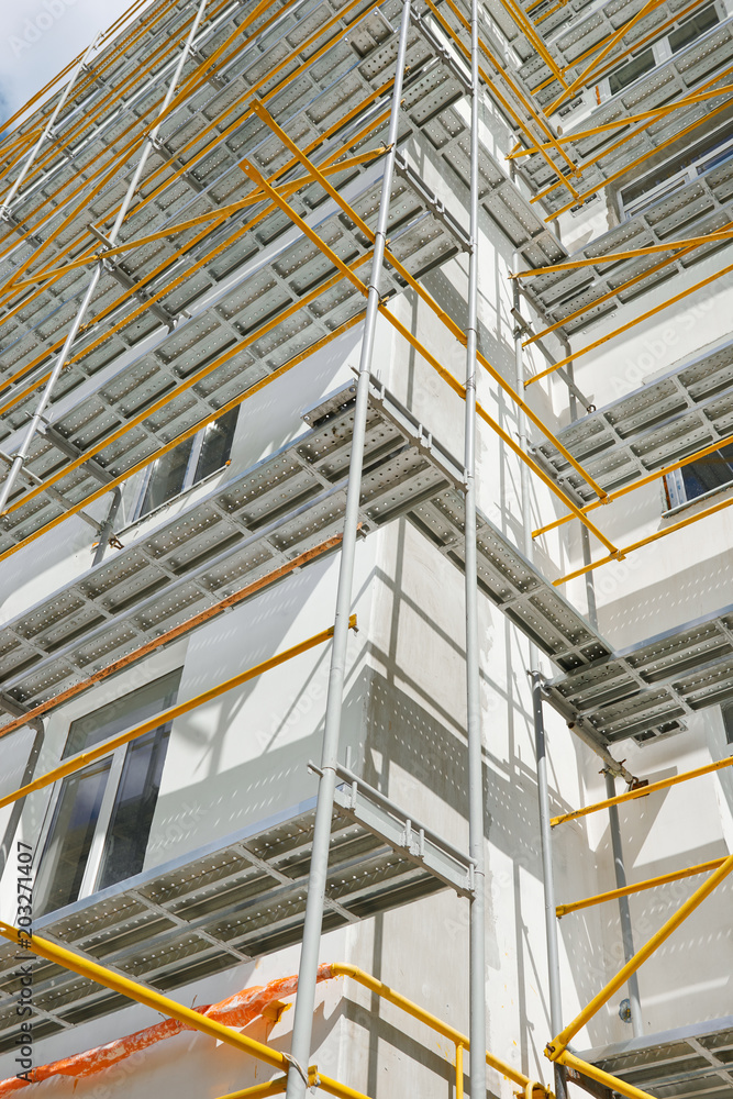 Fototapeta premium scaffolding near a new house, building exterior, construction and repair industry, white wall and window, yellow pipe