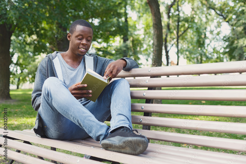 Young man reading book in park copy space Young man reading book in park copy space