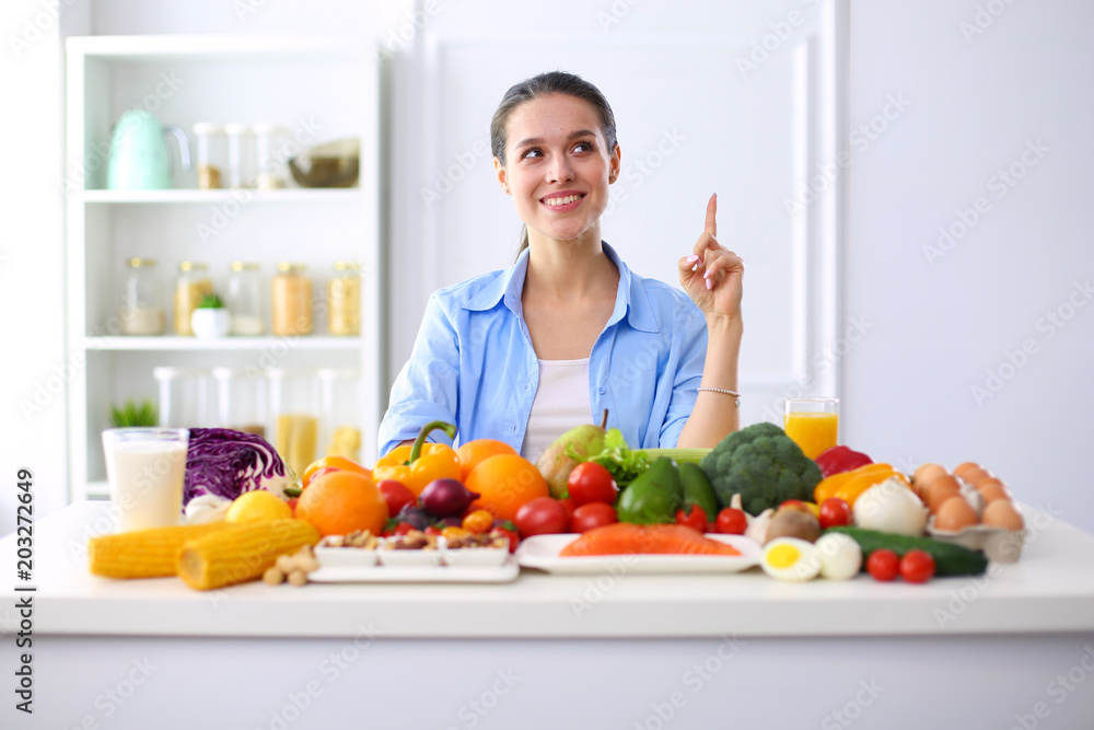 Young and cute woman sitting at the table full of fruits and vegetables in the wooden interior Young and cute woman sitting at the table full of fruits and vegetables in the wooden interior