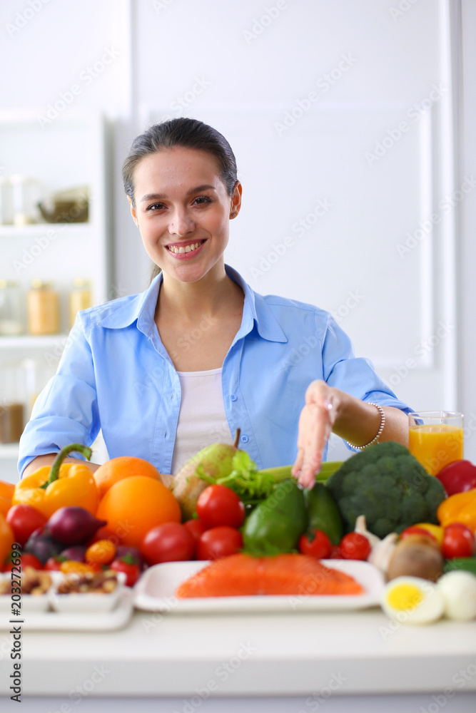 Young and cute woman sitting at the table full of fruits and vegetables in the wooden interior