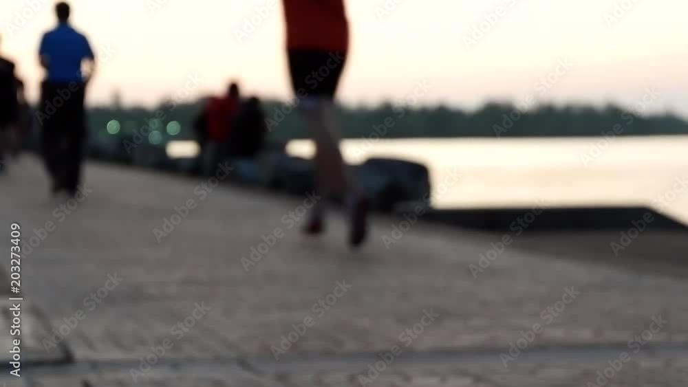 Blurred of people are running, walking and exercising in park with evening sunset and riverside background. Defocused of people outdoor activity background in spring and summer season.