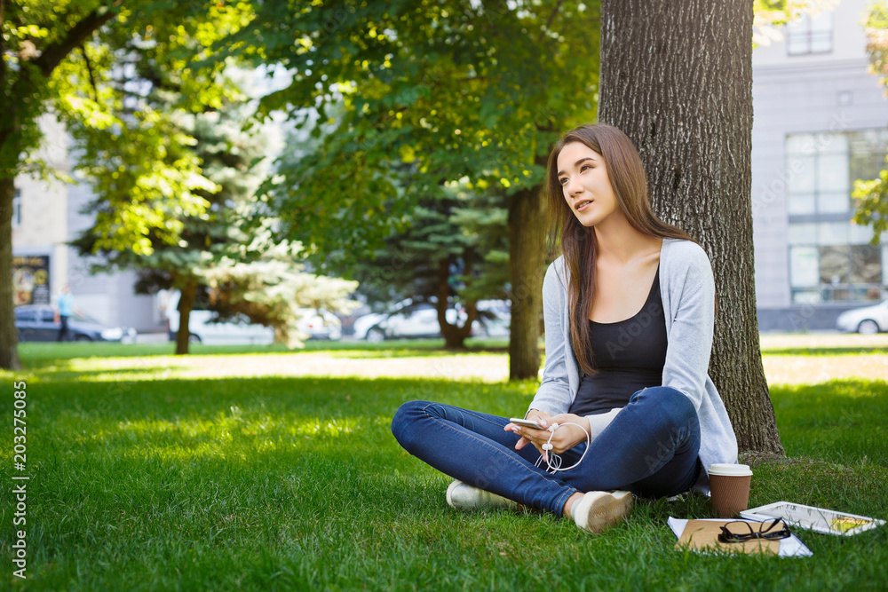 Young brunette asian girl relaxing on a grass and drinking coffee in the park during the day Young brunette asian girl relaxing on a grass and drinking coffee in the park during the day