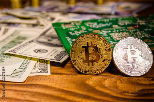 Bitcoins, circuit board and one hundred dollar bills on a wooden table