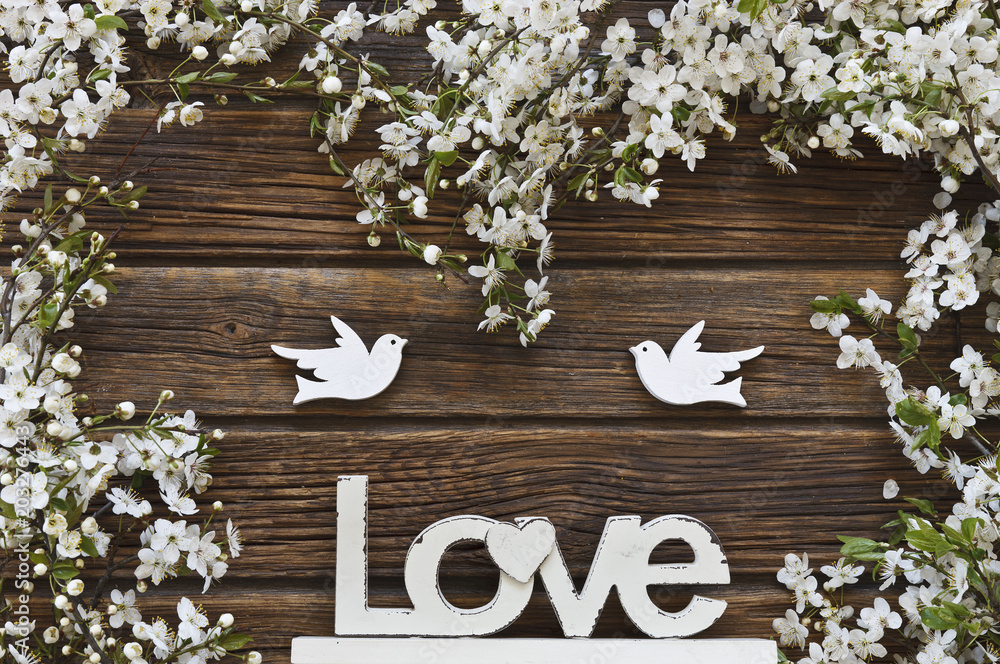 Naklejka premium Close-up photo of Beautiful white Flowering Cherry Tree branches with two wooden birds and letters love. Wedding, engagement or betrothal concept on vintage wooden background. Top view, greating card.