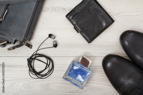Pair of black leather men's shoes, leather shoulder bag for men, men's cologne, headphones and purse on wooden background