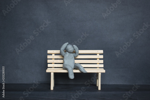 Tableau sur toile Sad plasticine man on a wooden bench on the dark background.