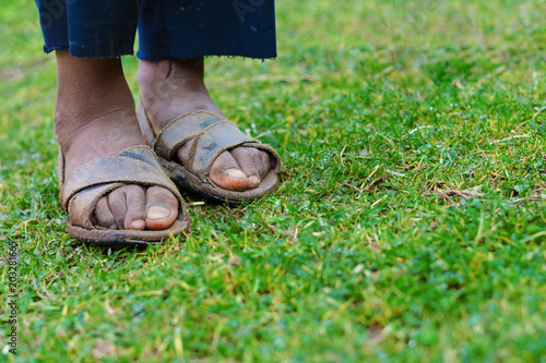 Feet of poor kid wearing dirty shoes standing on the grass.