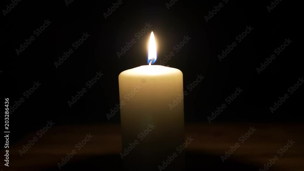 Lit white wax candle burning in a dark room - close up Lit white wax candle burning in a dark room - close up