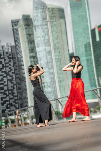 Two beautiful young girls having fun photo shooting on a deck with skyscrapers city background