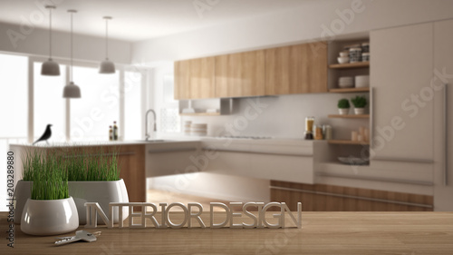 Wooden table or shelf with potted grass plant  house keys and 3D letters making the words interior design  over blurred modern kitchen  project concept architecture background