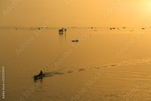 Silhouette of fisherman with his boat in the sea during sunrise.