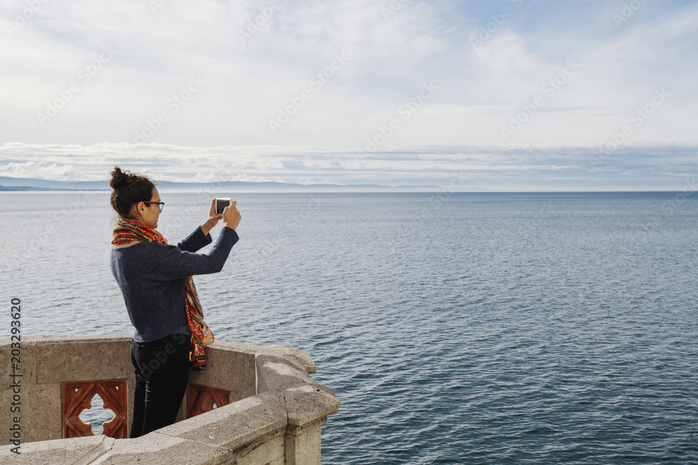 Woman photographing sea with smartphone while standing on terrace Woman photographing sea with smartphone while standing on terrace