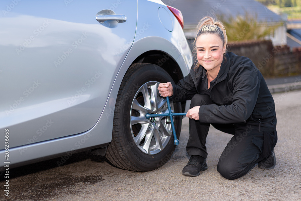 A woman mechanic loosening nuts on a wheel for a tire change, whilst looking at camera