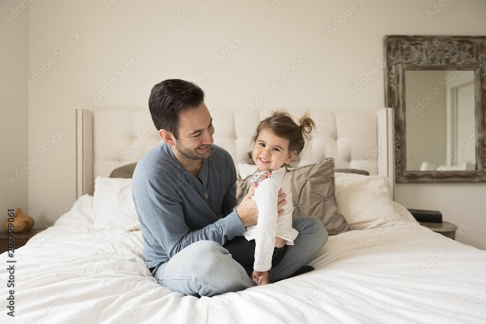 Smiling father with daughter siting on bed at home Smiling father with daughter siting on bed at home