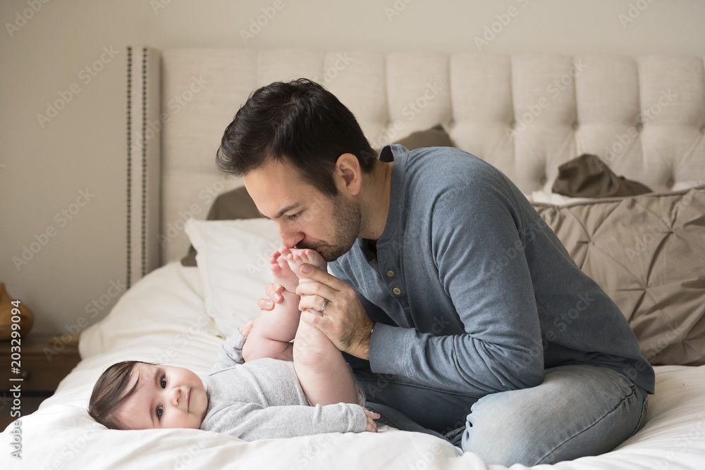 Father kissing son's feet while sitting on bed at home Father kissing son's feet while sitting on bed at home
