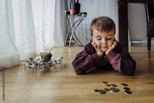 Boy with coins lying on floor at home photo