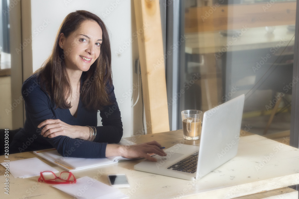 Woman working with her laptop sitting, looking camera having coffee inside a coffee shop. Woman working with her laptop sitting, looking camera having coffee inside a coffee shop.