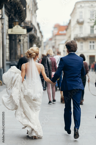 Romantic couple on a walk in the city, newlywed bride and groom walking outdoors in wedding clothing after ceremony, happy couple enjoying life © sonyachny