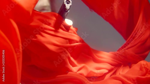 Close up shot of a man holding a firearm underwater behind falling red dress. photo