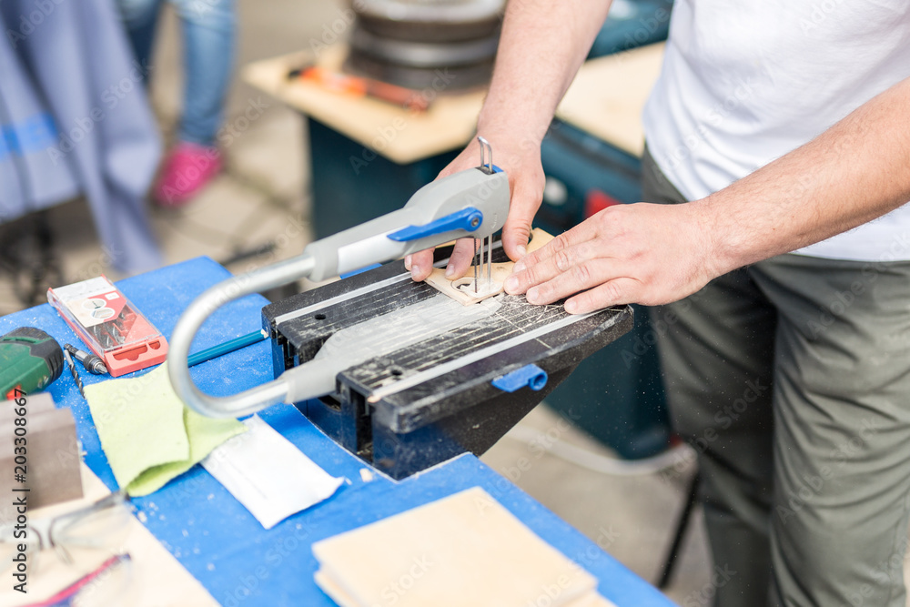 Man working with jig saw. Fretsaw tool stationary fixed on table. Person making wooden figures with electric saw tool Man working with jig saw. Fretsaw tool stationary fixed on table. Person making wooden figures with electric saw tool