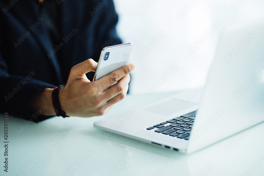 close up of businessman using mobile phone and laptop computer on desk in modern office close up of businessman using mobile phone and laptop computer on desk in modern office