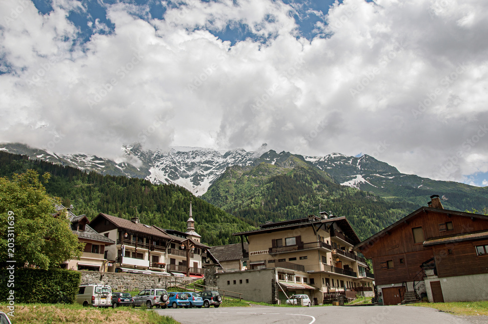 Houses and bellow tower in front of snowy mountains in a sunny day at Les-Contamines-Montjoie. A small alpine village located in the Haute-Savoie Province, near the Mont Blanc in the French Alps.