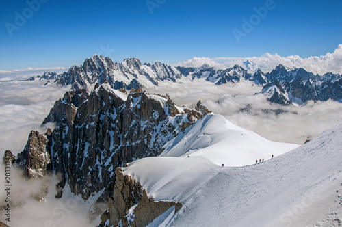 Snowy peaks and mountaineers in a sunny day, viewed from the Aiguille du Midi, near Chamonix. A famous ski resort located in Haute-Savoie Province, at the foot of Mont Blanc in the French Alps.