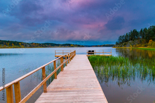 The pier on the lake. Empty dock on sunset background. A wooden bridge near the water. © Grispb